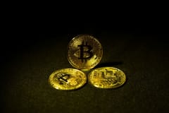 Three gold bitcoin coins displayed on a dark, textured surface highlighting cryptocurrency symbolism.