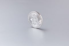 Close-up of a silver Bitcoin coin standing upright against a clean, white background.