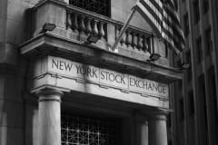 Black and white photo of the New York Stock Exchange facade with USA flag.