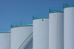 Large industrial storage tanks with green railings against a clear blue sky.