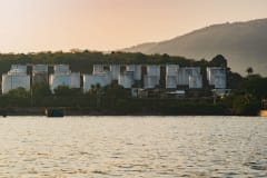 A picturesque view of industrial oil storage tanks set against a serene lake with mountains in the background.