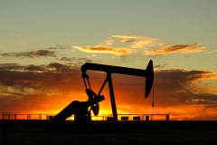 Dramatic silhouette of an oil pump jack against a vibrant sunset sky, emphasizing energy extraction.