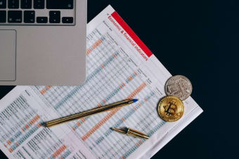 Top view of bitcoin coins on financial documents beside a laptop keyboard.