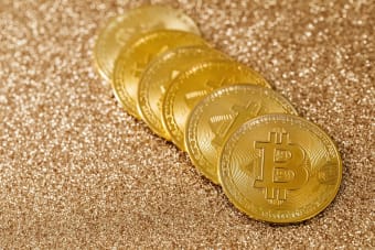 A stack of gold Bitcoin coins placed on a shimmering gold glitter background.
