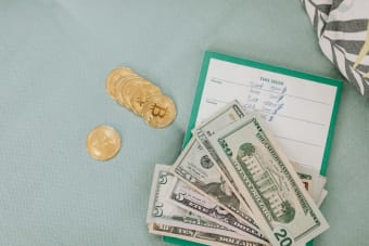 Close-up of U.S. dollars and Bitcoin coins placed on a weekly budget planner, symbolizing modern finance.
