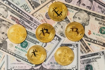 Gold bitcoins placed on a background of US dollar bills representing cryptocurrency and traditional finance.