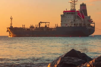Large oil tanker on the ocean near the coast, sailing under a vibrant sunset sky.