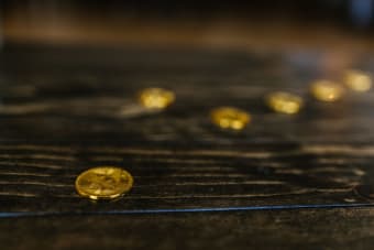 Close-up of multiple gold Bitcoin coins on a wooden table, representing wealth and cryptocurrency.