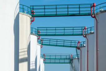 Modern industrial storage tanks with walkways against a clear blue sky.