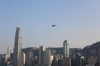 A helicopter flies above the iconic Hong Kong skyline during the day.