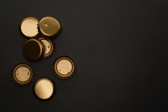 Flat lay of golden metallic bottle caps on a black background, offering copyspace.