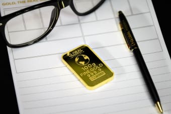 Gold bullion on notepad with eyeglasses and pen, symbolizing wealth and business planning.