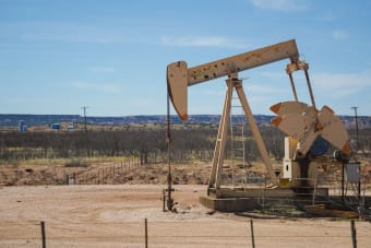Industrial oil pumpjack in a desert setting under a clear blue sky, illustrating oil extraction technology.