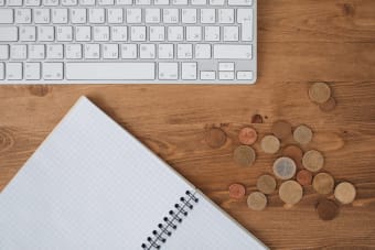 Flat lay of a desk featuring a keyboard, notebook, and scattered coins on a wooden surface.