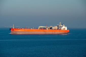 Bright orange LNG carrier ship cruising through calm sea waters on a clear day.