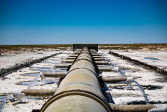 Large industrial pipeline discharging wastewater in arid, rural landscape under clear blue sky.