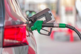 A close-up view of a fuel pump nozzle inserted into a car's tank at a gas station.