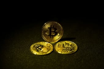 Three gold bitcoin coins displayed on a dark, textured surface highlighting cryptocurrency symbolism.