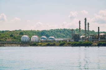 A scenic view of a coastal industrial gas storage facility with spherical tanks and tall chimneys.