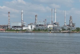 A large oil refinery complex next to the water with cloudy skies.