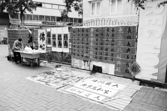 Grayscale photo of a street calligraphy stall in Hong Kong, showcasing Chinese characters.