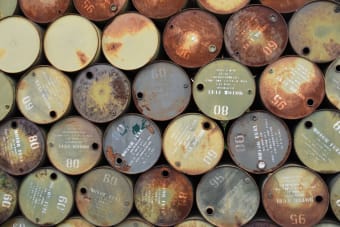 Pile of old, rusty oil barrels stacked outdoors with visible labels and numbers.