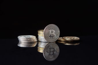 Silver bitcoins stacked on a reflective surface with a dark background, symbolizing cryptocurrency and digital wealth.