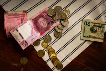 Image of Peruvian banknotes and US dollar bills with scattered coins on a striped surface.