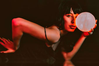 A mysterious woman holding a glowing orb in a dark setting with artistic lighting.