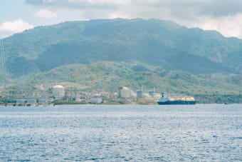Coastal industrial facility with a tanker ship against a mountainous backdrop.