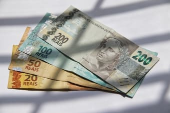 Various Brazilian real banknotes in sunlight, showcasing currency variety.