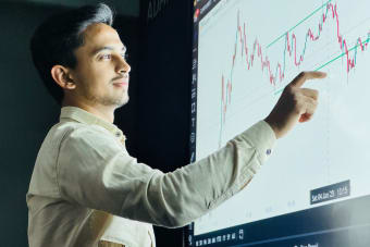 Man analyzing stock market graph on a digital board with a focused expression.