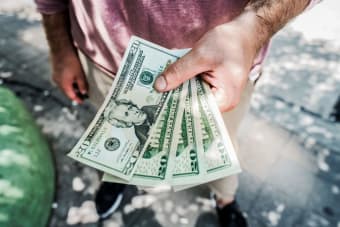A person holding several twenty-dollar bills outdoors, depicting payment or financial transaction.