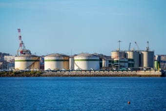 Large storage tanks at an industrial port facility by the water under clear blue skies.