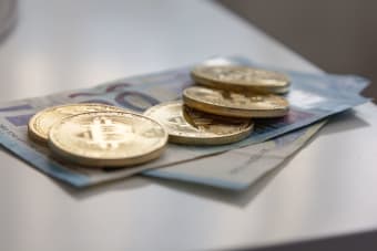 A close-up image showing Bitcoin coins placed on Euro banknotes, highlighting finance and cryptocurrency.