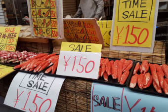 Outdoor market stall featuring seafood and beef skewers on sale with vibrant signage in Japanese Yen.