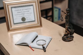 A framed certificate with Lady Justice statue on a wooden desk.