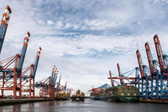 Wide view of container ships and cranes at Hamburg port under a cloudy sky.