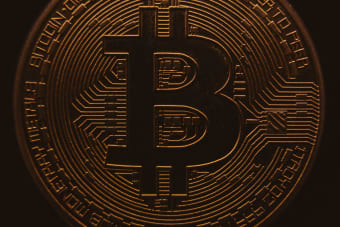 Close-up view of a bitcoin coin showing its intricate, digital design in a warm, dark ambiance.