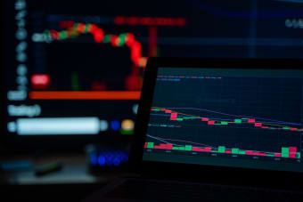 A dimly lit desk setup displaying cryptocurrency trading charts on multiple screens.