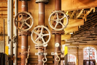 Close-up of rusty industrial pipes and valves, showcasing aging machinery in a factory setting.