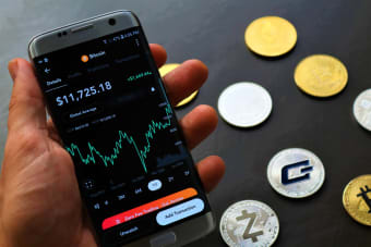 Close-up of a smartphone app showing Bitcoin trading details with crypto coins on a black surface.