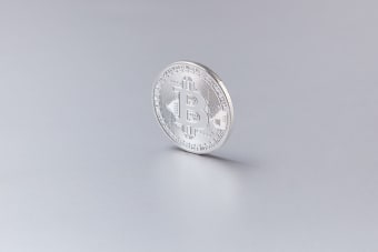 Close-up of a silver Bitcoin coin standing upright against a clean, white background.