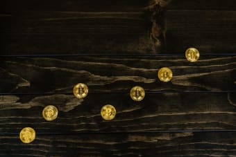 Gold-colored bitcoins arranged diagonally on a dark wooden surface.