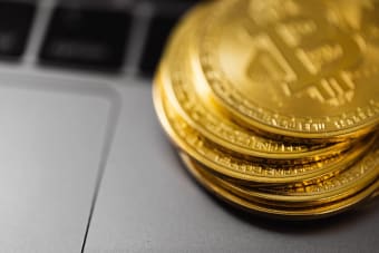 Stack of gold Bitcoin coins on a laptop keyboard, symbolizing digital currency technology and wealth.
