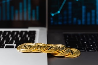 Gold bitcoins placed on laptop keyboards with digital financial graphs in the background.