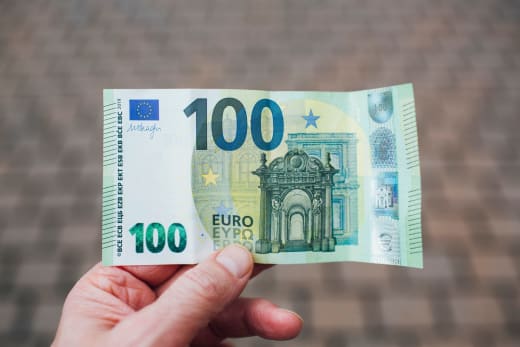 Close-up photo showing a person holding a 100 euro banknote against a blurred background.