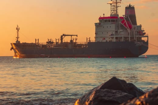 Large oil tanker on the ocean near the coast, sailing under a vibrant sunset sky.