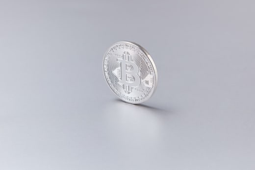Close-up of a silver Bitcoin coin standing upright against a clean, white background.
