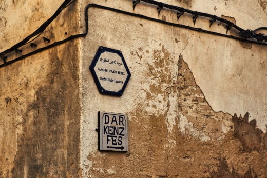 Street signs on a rustic wall in the medina of Fes, Morocco, showcasing cultural heritage.